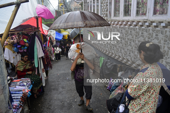 A man is carrying a heavy load on his head with an umbrella during rainfall in Darjeeling, India, on July 2, 2024. A woman is carrying heavy...