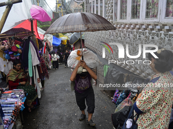 A man is carrying a heavy load on his head with an umbrella during rainfall in Darjeeling, India, on July 2, 2024. A woman is carrying heavy...