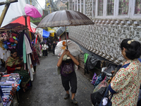 A man is carrying a heavy load on his head with an umbrella during rainfall in Darjeeling, India, on July 2, 2024. A woman is carrying heavy...