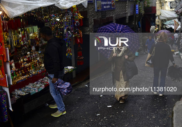 A woman is carrying an umbrella in a marketplace during rainfall in Darjeeling, India, on July 2, 2024. A woman is carrying heavy loads on h...