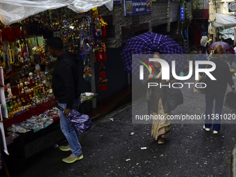 A woman is carrying an umbrella in a marketplace during rainfall in Darjeeling, India, on July 2, 2024. A woman is carrying heavy loads on h...