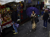 A woman is carrying an umbrella in a marketplace during rainfall in Darjeeling, India, on July 2, 2024. A woman is carrying heavy loads on h...