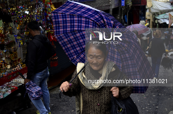 A woman is carrying an umbrella in a marketplace during rainfall in Darjeeling, India, on July 2, 2024. A woman is carrying heavy loads on h...