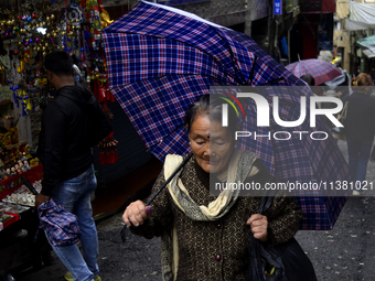 A woman is carrying an umbrella in a marketplace during rainfall in Darjeeling, India, on July 2, 2024. A woman is carrying heavy loads on h...