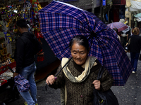 A woman is carrying an umbrella in a marketplace during rainfall in Darjeeling, India, on July 2, 2024. A woman is carrying heavy loads on h...