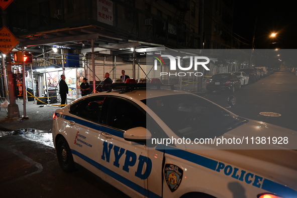 A New York City Police Department vehicle is blocking the roadway at the crime scene. One person is being assaulted, and one person is being...