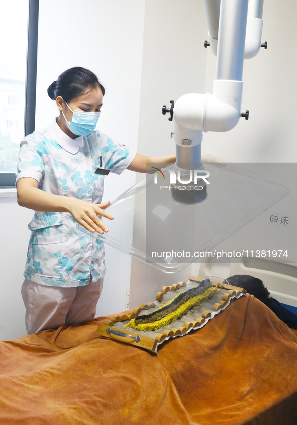 A doctor in the department of acupuncture and massage at a traditional Chinese medicine hospital is giving a person a moxibustion to help hi...