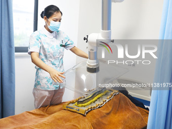 A doctor in the department of acupuncture and massage at a traditional Chinese medicine hospital is giving a person a moxibustion to help hi...