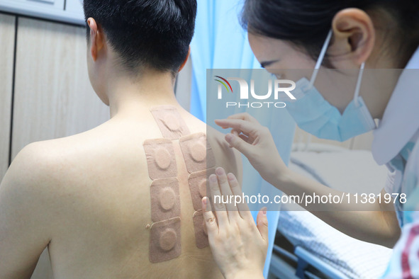 A doctor in the department of acupuncture and massage at a traditional Chinese Medicine hospital is applying the ''Sanfu Patch'' to citizens...