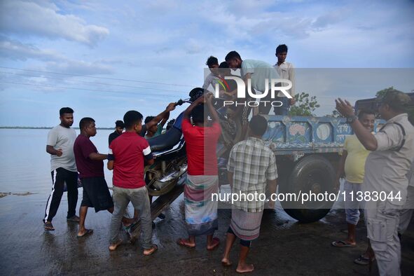 People are trying to load a bike onto a tractor to cross a flooded road after heavy rainfall in Hojai District of Assam, India, on July 5, 2...