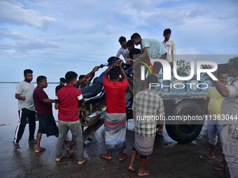 People are trying to load a bike onto a tractor to cross a flooded road after heavy rainfall in Hojai District of Assam, India, on July 5, 2...