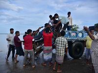 People are trying to load a bike onto a tractor to cross a flooded road after heavy rainfall in Hojai District of Assam, India, on July 5, 2...