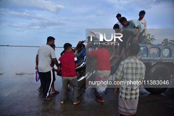 People are trying to load a bike onto a tractor to cross a flooded road after heavy rainfall in Hojai District of Assam, India, on July 5, 2...