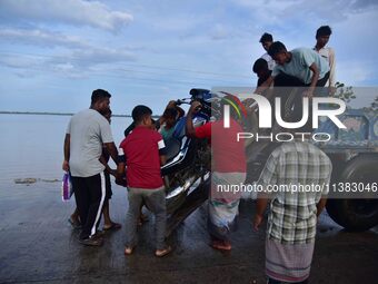 People are trying to load a bike onto a tractor to cross a flooded road after heavy rainfall in Hojai District of Assam, India, on July 5, 2...