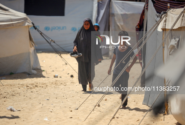 Displaced Palestinians are walking next to a temporary camp in Khan Yunis, south of the Gaza Strip, on July 4, 2024, amid the ongoing confli...