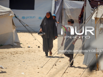 Displaced Palestinians are walking next to a temporary camp in Khan Yunis, south of the Gaza Strip, on July 4, 2024, amid the ongoing confli...