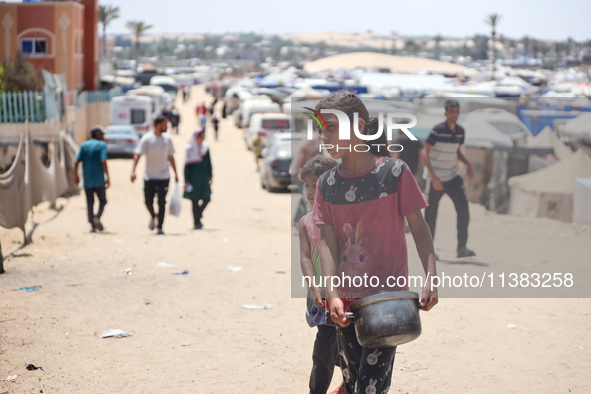 Displaced Palestinians are walking next to a temporary camp in Khan Yunis, south of the Gaza Strip, on July 4, 2024, amid the ongoing confli...