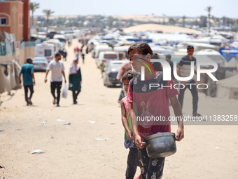 Displaced Palestinians are walking next to a temporary camp in Khan Yunis, south of the Gaza Strip, on July 4, 2024, amid the ongoing confli...