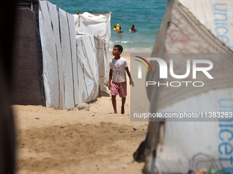 Displaced Palestinians are walking next to a temporary camp in Khan Yunis, south of the Gaza Strip, on July 4, 2024, amid the ongoing confli...