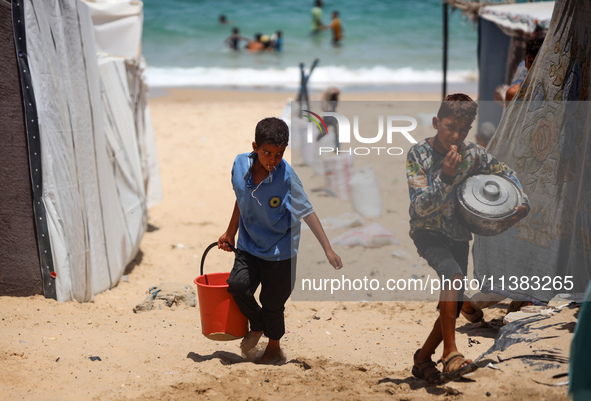 Displaced Palestinians are walking next to a temporary camp in Khan Yunis, south of the Gaza Strip, on July 4, 2024, amid the ongoing confli...