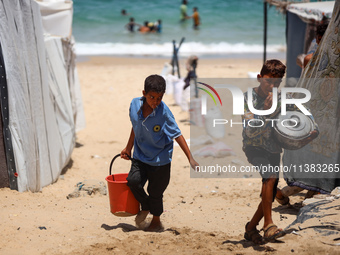 Displaced Palestinians are walking next to a temporary camp in Khan Yunis, south of the Gaza Strip, on July 4, 2024, amid the ongoing confli...