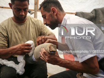 Muattaz Abu Dayeh, a physiotherapist, is applying a medical prosthesis to 32-year-old worker Majd al-Omari, who lost part of his leg during...