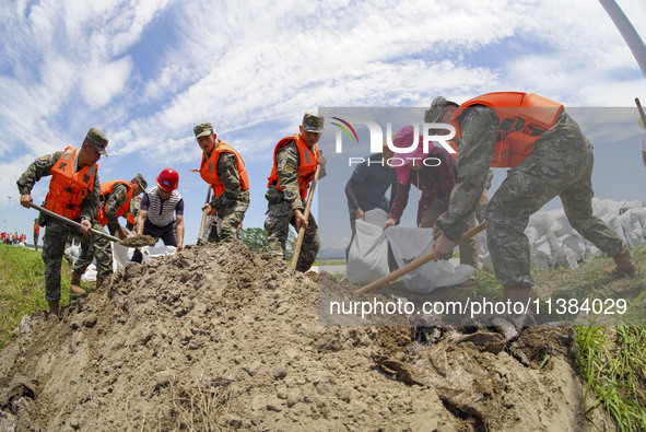 Armed police officers and soldiers are filling sandbags for flood control at the Changjiang River embankment section of Rixin village, Mianc...