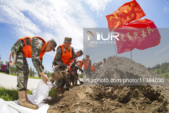 Armed police officers and soldiers are filling sandbags for flood control at the Changjiang River embankment section of Rixin village, Mianc...