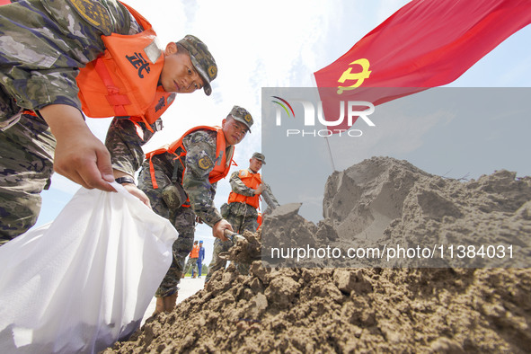 Armed police officers and soldiers are filling sandbags for flood control at the Changjiang River embankment section of Rixin village, Mianc...