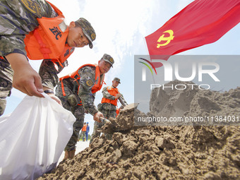 Armed police officers and soldiers are filling sandbags for flood control at the Changjiang River embankment section of Rixin village, Mianc...