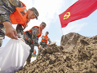 Armed police officers and soldiers are filling sandbags for flood control at the Changjiang River embankment section of Rixin village, Mianc...