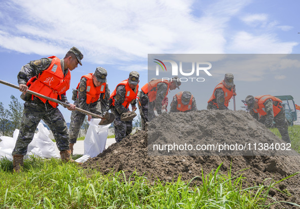 Armed police officers and soldiers are filling sandbags for flood control at the Changjiang River embankment section of Rixin village, Mianc...