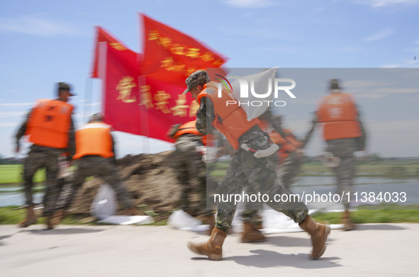 Armed police officers and soldiers are filling sandbags for flood control at the Changjiang River embankment section of Rixin village, Mianc...