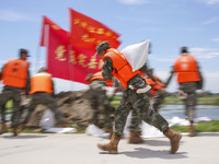 Armed police officers and soldiers are filling sandbags for flood control at the Changjiang River embankment section of Rixin village, Mianc...