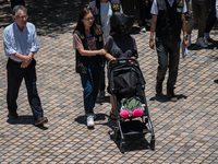 Police officers are escorting a suspect involved in a kidnapping case, who is wearing a head cover and pushing a baby stroller with a doll i...