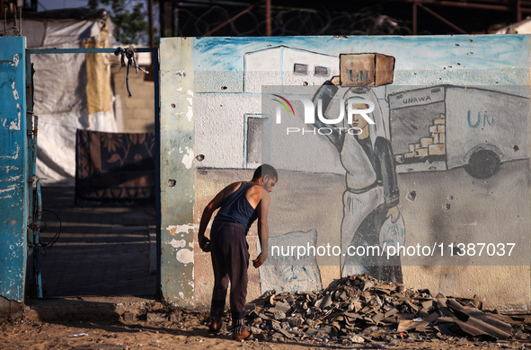 A displaced Palestinian is walking past the UNRWA Deir el-Balah distribution center, in Deir el-Balah in the central Gaza Strip, on July 6,...