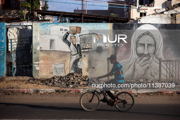 A Palestinian man is riding a bicycle past the UNRWA Deir el-Balah distribution center, in Deir el-Balah in the central Gaza Strip, on July...