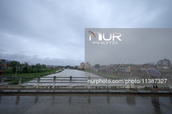 A Nepali citizen is wearing an umbrella and watching the rising level of the Bagmati River in Lalitpur, Nepal, on July 6, 2024. With the ons...