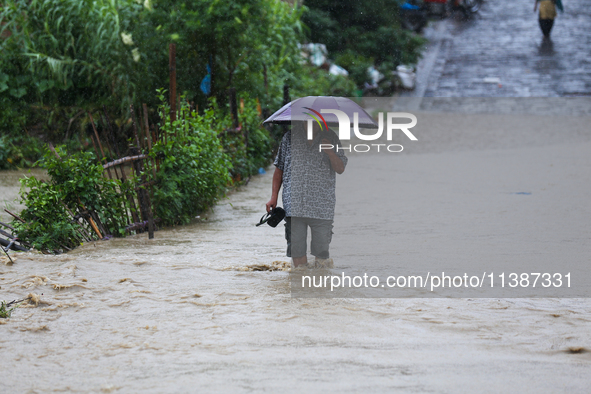 A Nepali man is wading through a river that has burst its embankment and is flowing into the residential areas in Bhaktapur, Nepal, on July...