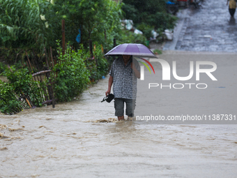 A Nepali man is wading through a river that has burst its embankment and is flowing into the residential areas in Bhaktapur, Nepal, on July...