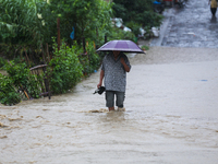 A Nepali man is wading through a river that has burst its embankment and is flowing into the residential areas in Bhaktapur, Nepal, on July...