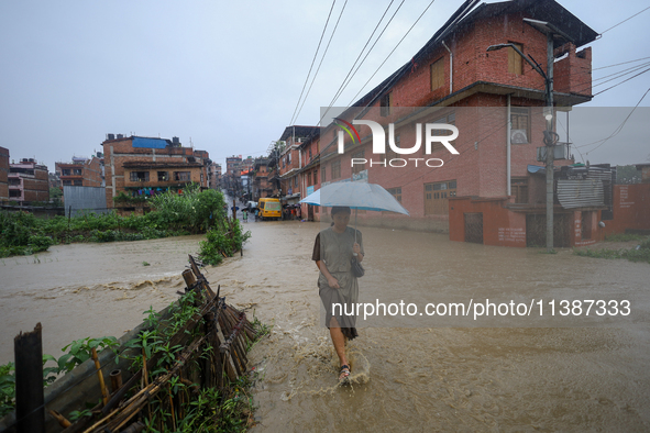 A Nepali woman is wading through a river that has burst its embankment and flowed into the residential areas in Bhaktapur, Nepal, on July 6,...