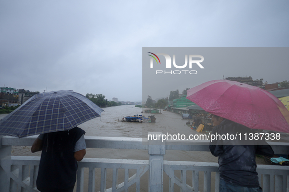 Nepali citizens are watching the rising level of Bagmati River while standing over a bridge in Kathmandu, Nepal, on July 6, 2024. 