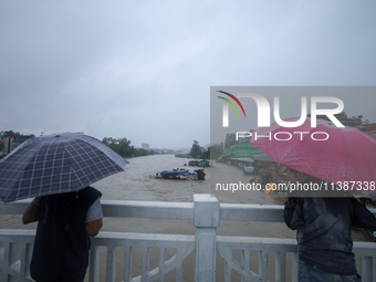 Nepali citizens are watching the rising level of Bagmati River while standing over a bridge in Kathmandu, Nepal, on July 6, 2024. (