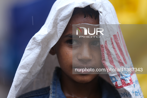 A Nepali boy is covering himself with a sack during the heavy rains in Nepal, on July 6, 2024. 