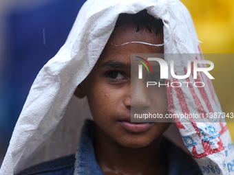 A Nepali boy is covering himself with a sack during the heavy rains in Nepal, on July 6, 2024. (