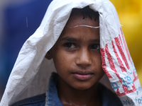 A Nepali boy is covering himself with a sack during the heavy rains in Nepal, on July 6, 2024. (