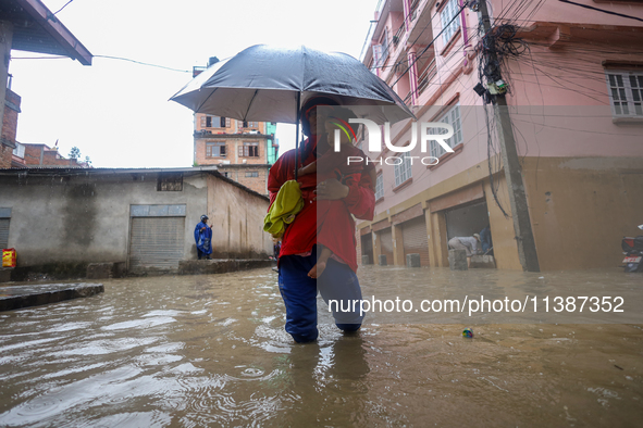 A Nepali man is carrying his child and wading through the flooded water in Kathmandu, Nepal, on July 6, 2024. 