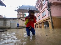 A Nepali man is carrying his child and wading through the flooded water in Kathmandu, Nepal, on July 6, 2024. (