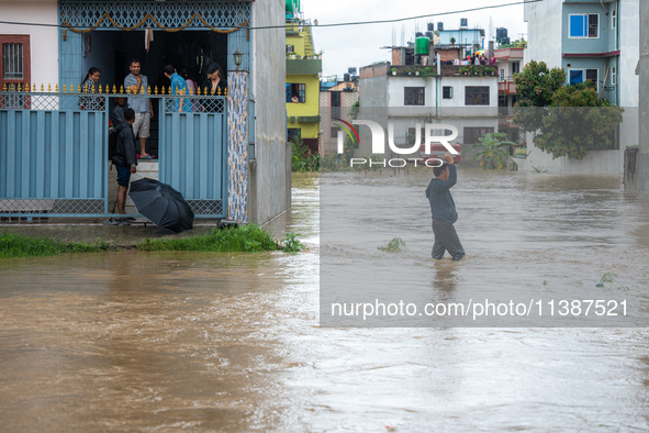 A man is attempting to cross a flooded road with his belongings packed in a suitcase in Tikathali, Kathmandu, on July 6, 2024, following inc...